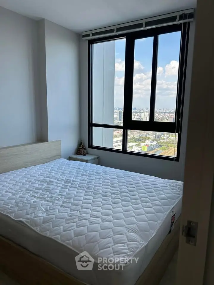 Bright bedroom with large window offering stunning city views, featuring a comfortable bed and modern decor.