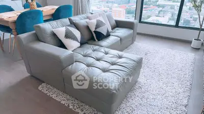 Modern living room with stylish gray leather sofa and city view from large window.