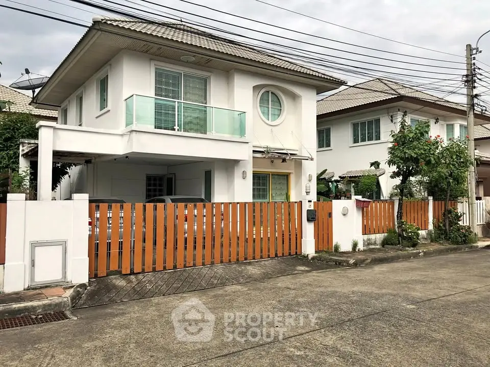 Charming two-story house with balcony and gated driveway in a suburban neighborhood.