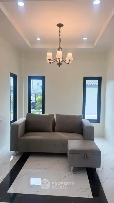 Modern living room with elegant chandelier and cozy gray sofa, featuring large windows for natural light.