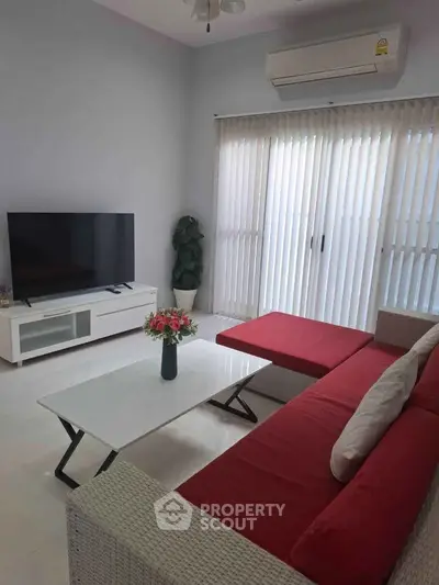 Modern living room with red sofa, flat-screen TV, and air conditioning in a bright space.