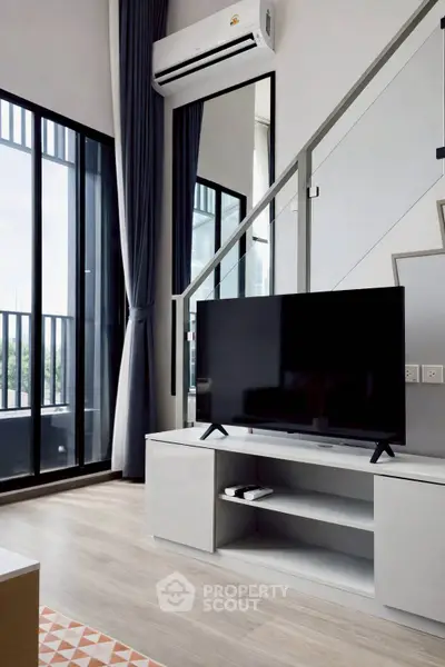 Modern living room with large windows and sleek TV setup in a stylish apartment.