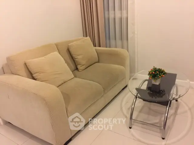 Cozy living room with beige sofa and glass coffee table, perfect for relaxation.