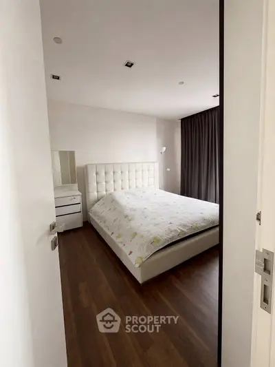 Modern bedroom with elegant decor and wooden flooring, featuring a plush bed and stylish curtains.