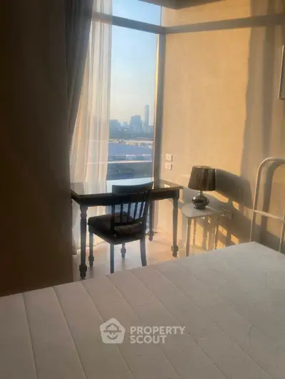 Cozy bedroom with city view, featuring a desk and lamp by the window.