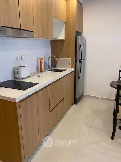 Modern kitchen with sleek wooden cabinets, stainless steel fridge, and electric cooktop in a compact layout.