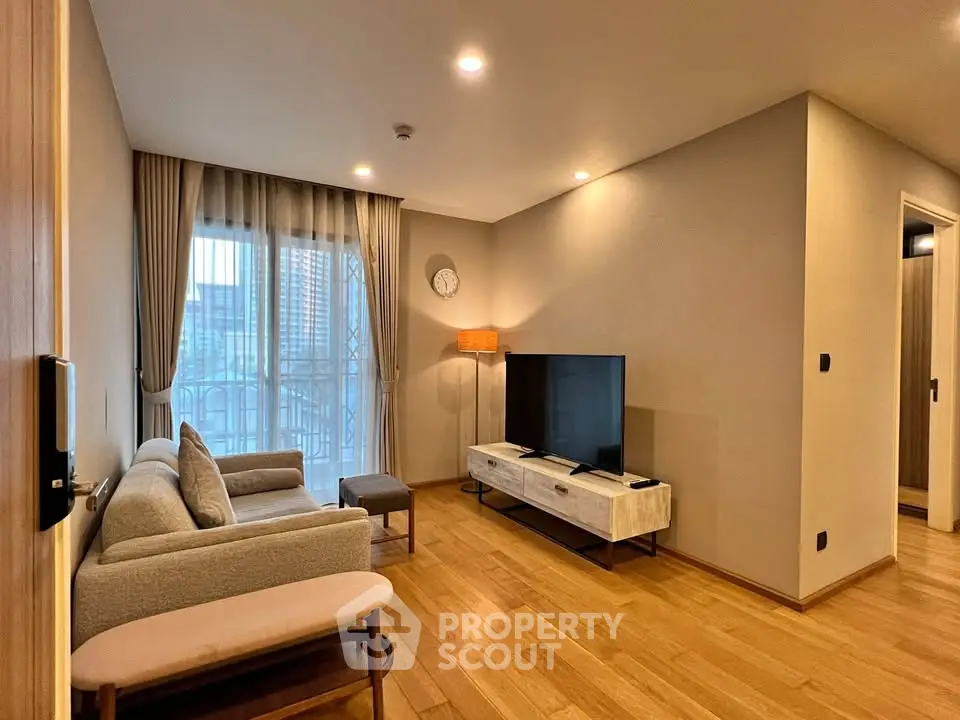Modern living room with wooden flooring, cozy sofa, and large TV, featuring elegant curtains and soft lighting.