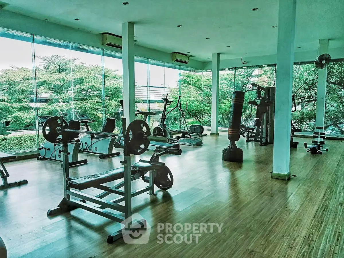 Spacious gym with modern equipment and large windows offering lush green views.