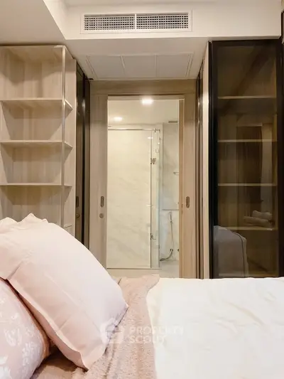 Modern bedroom with sliding glass doors leading to a stylish bathroom, featuring elegant shelving and soft bedding.