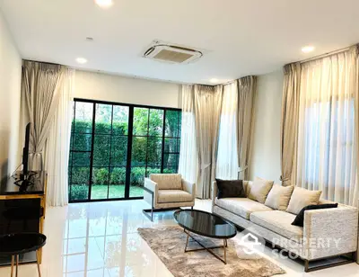 Spacious living room with polished tile flooring, elegant drapery, and abundant natural light from floor-to-ceiling windows overlooking greenery.