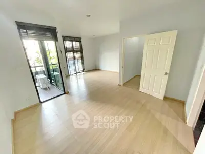 Spacious empty room with wooden flooring and balcony access in modern apartment.