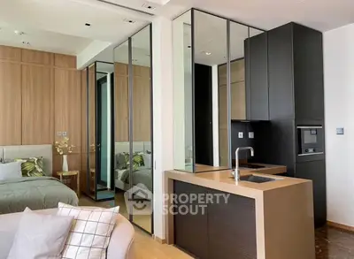 Modern studio apartment with sleek kitchen and cozy bedroom area, featuring mirrored walls and stylish decor.