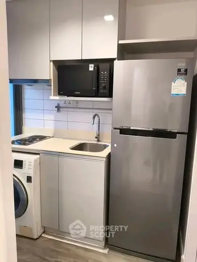 Modern compact kitchen with fridge, microwave, and washing machine in sleek apartment.