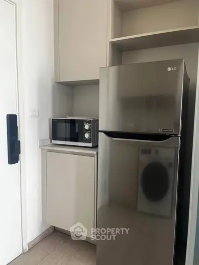 Modern kitchen with stainless steel fridge and microwave in compact layout.