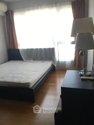 Cozy bedroom with natural light, wooden flooring, and modern furnishings in a stylish apartment.