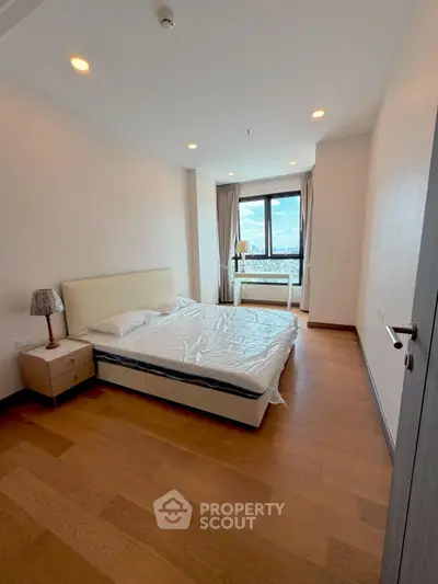 Spacious bedroom with wooden flooring and large window offering city views