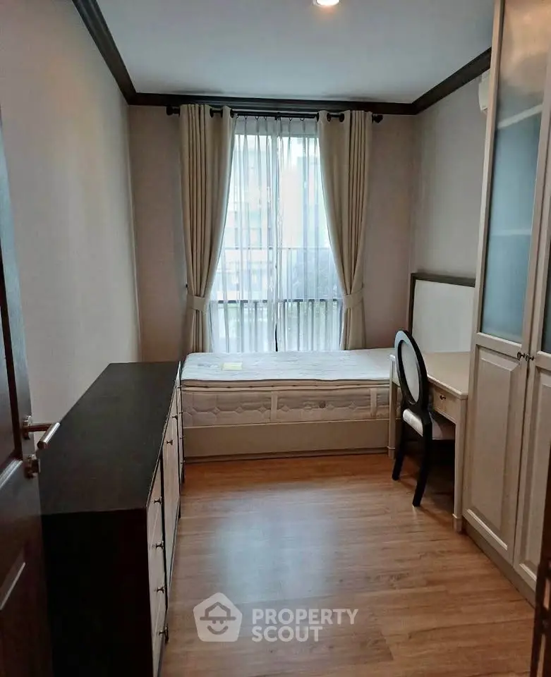 Cozy bedroom with wooden flooring, large window, and elegant furnishings in a modern apartment.