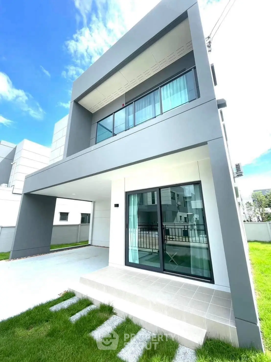 Modern two-story house with sleek design and large windows, featuring a spacious carport and lush green lawn.