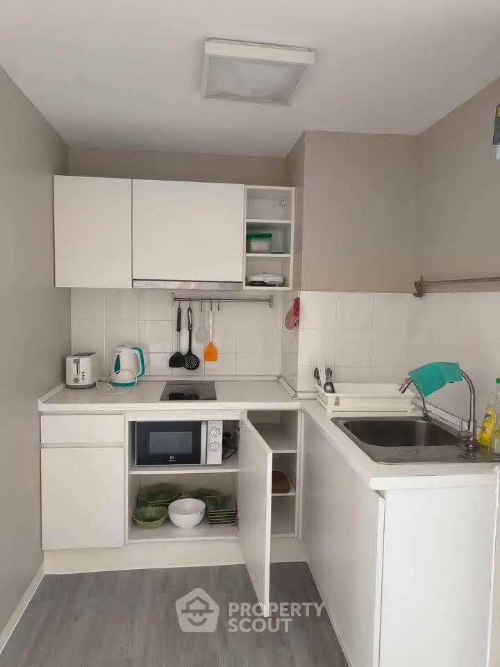 Compact modern kitchen with white cabinets and appliances, featuring a microwave and ample storage space.