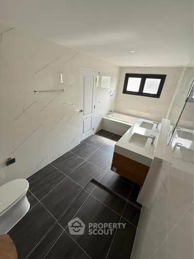 Spacious modern bathroom with dual sinks and bathtub, featuring sleek tile design and natural light.