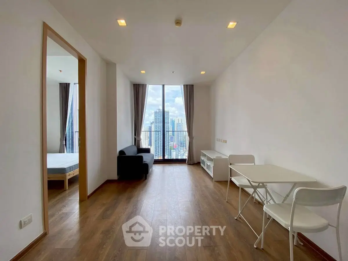 Modern living room with city view, featuring wooden flooring and minimalist furniture.