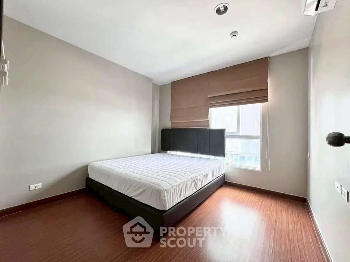 Spacious bedroom with large window and modern furnishings in a bright apartment.