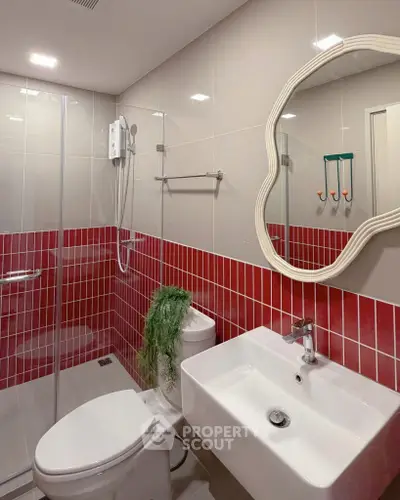 Modern bathroom with red tile accents and unique mirror design