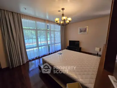 Spacious bedroom with large window and elegant chandelier in modern apartment.