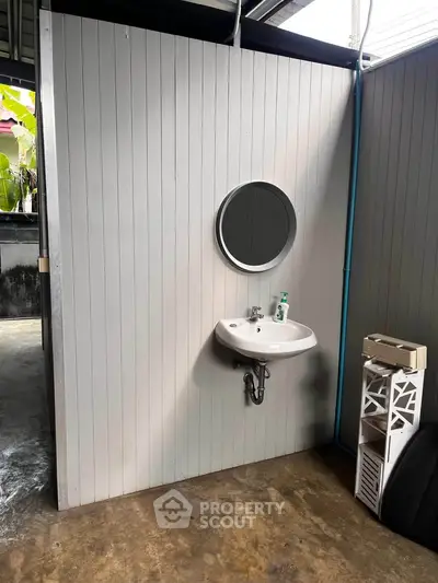 Minimalist bathroom with round mirror and white sink in industrial-style setting.