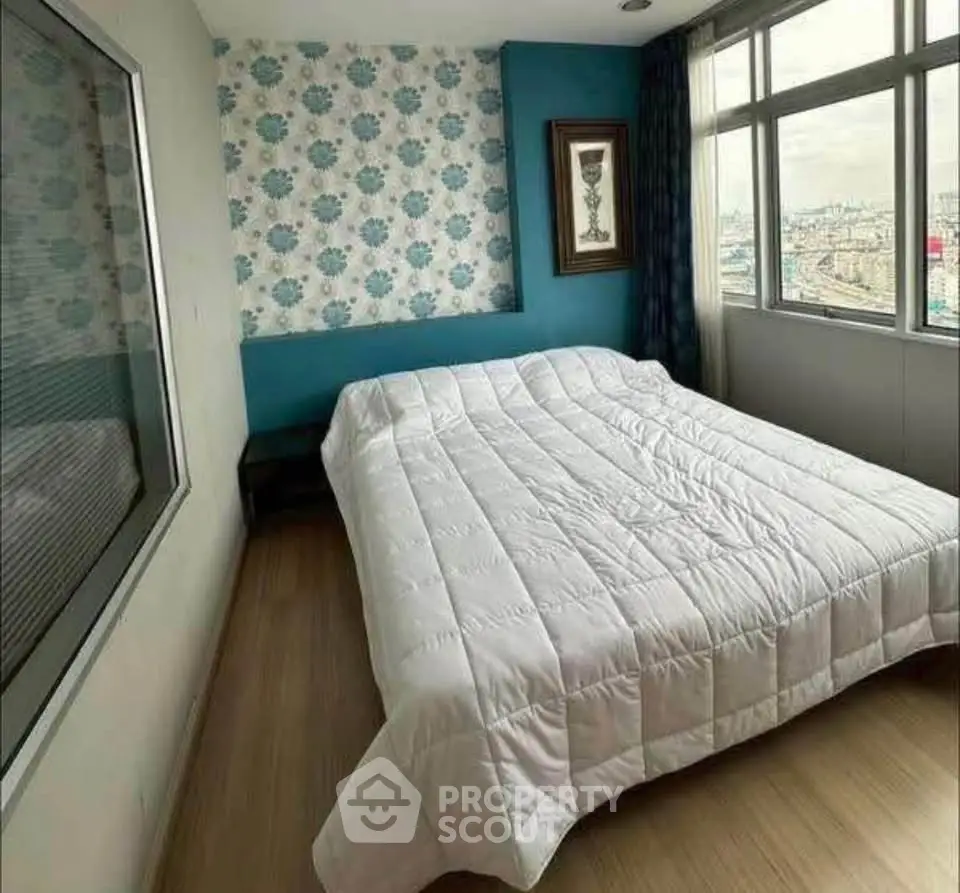 Cozy bedroom with large window offering city views, featuring modern decor and stylish wallpaper accent wall.