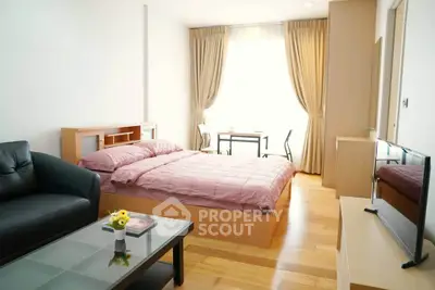 Modern studio apartment with cozy bed, stylish sofa, and natural light from large window.