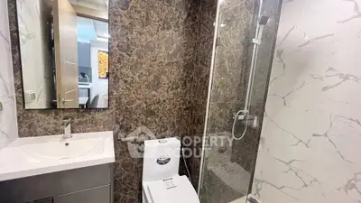 Modern bathroom with marble tiles and glass shower enclosure in luxury apartment.