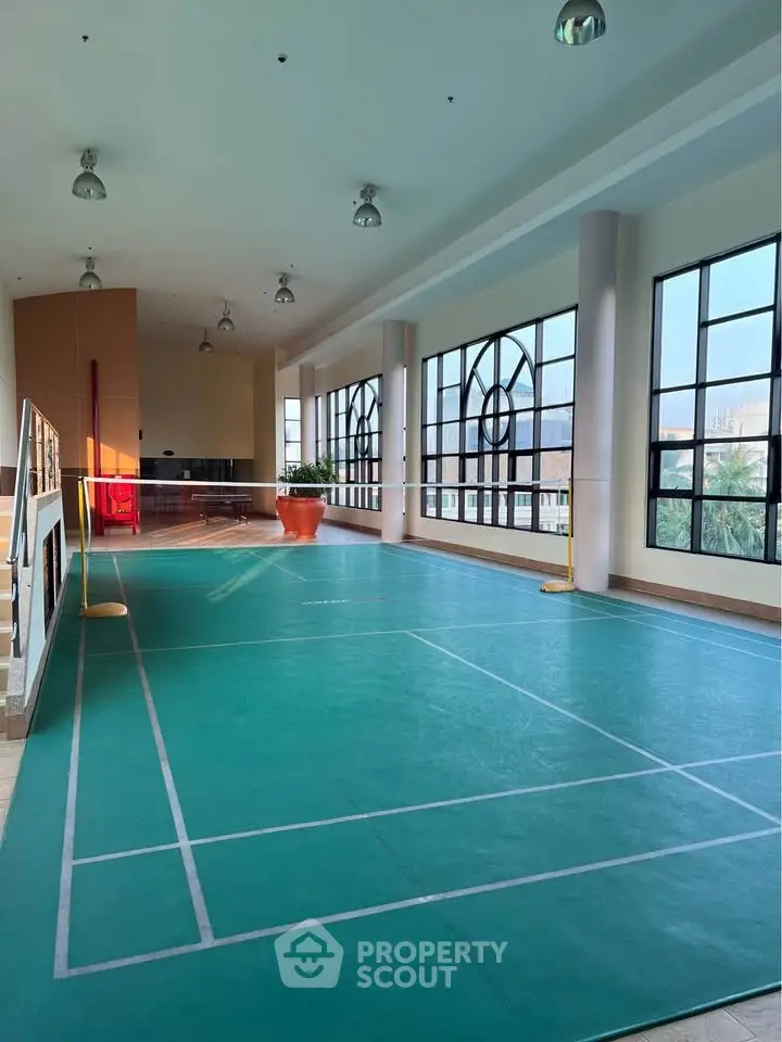 Spacious indoor badminton court with large windows and natural light in modern building.