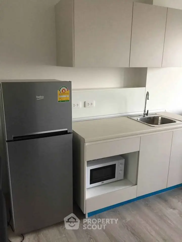 Modern kitchen with sleek cabinets, stainless steel fridge, and built-in microwave in a compact layout.