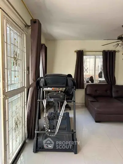 Spacious living room with treadmill and modern sofa, ample natural light through large windows.