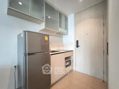 Modern compact kitchen with sleek cabinetry and stainless steel fridge in a stylish apartment.