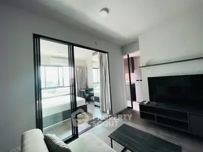 Modern apartment living room with TV and sliding glass doors to bedroom, featuring sleek design and natural light.