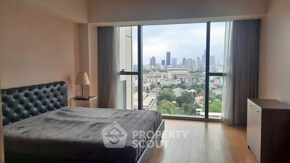 Spacious bedroom with stunning city view from large window, featuring modern furnishings and natural light.
