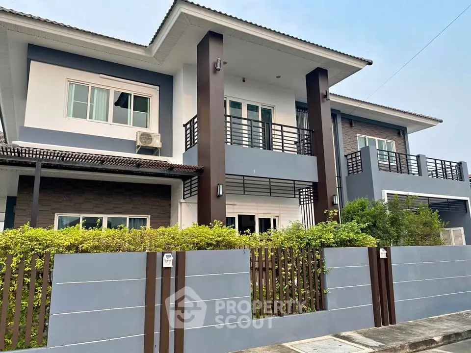 Modern two-story house with balcony and lush greenery in a serene neighborhood.