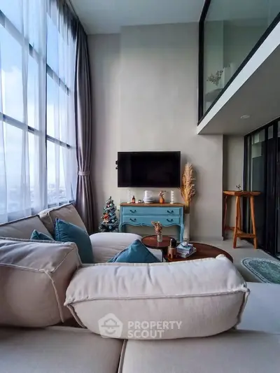 Modern living room with high ceilings and large windows, featuring cozy seating and stylish decor.