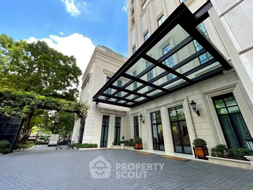 Elegant building entrance with glass canopy and lush greenery, perfect for luxury living.