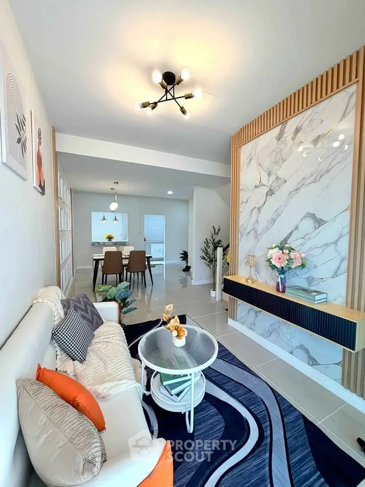 Modern living room with stylish decor and open dining area, featuring elegant marble accent wall and contemporary lighting.