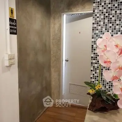 Chic modern hallway with textured walls and floral decor leading to a restroom.