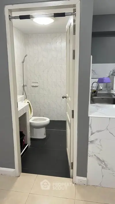 Compact bathroom with modern fixtures and adjacent kitchen area in a cozy apartment.