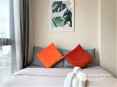 Cozy bedroom with a stylish grey bedspread and vibrant orange pillows, complemented by modern art and natural light.