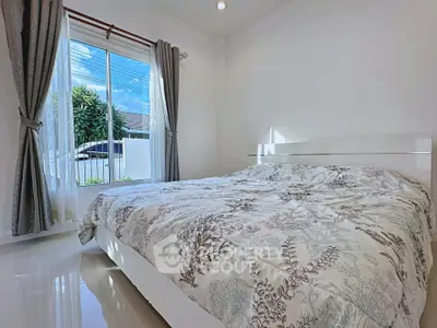 Bright bedroom with large window and elegant curtains, featuring a cozy bed with floral bedding.