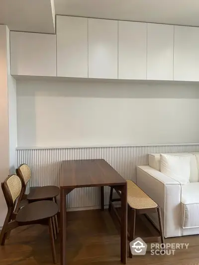 Modern dining area with sleek wooden table and chairs, white cabinetry, and cozy sofa.