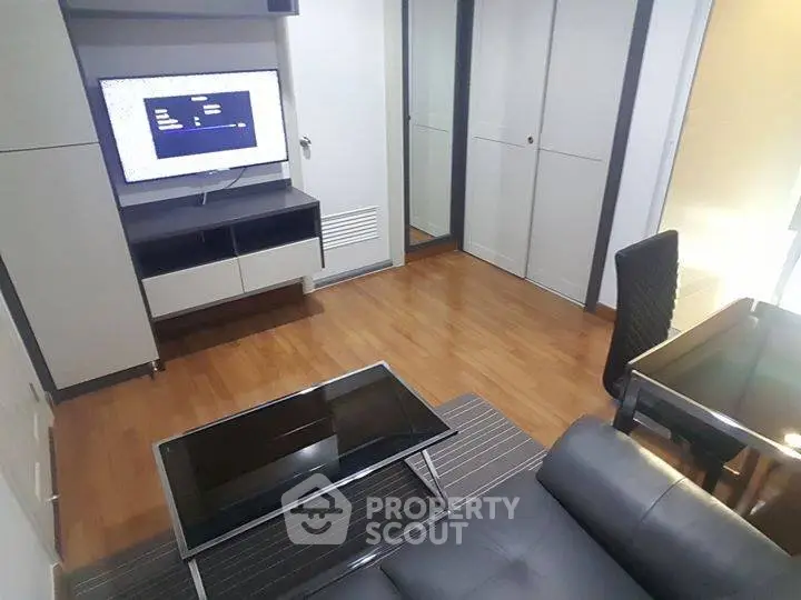 Modern living room with sleek furniture and wooden flooring, featuring a wall-mounted TV and glass dining table.