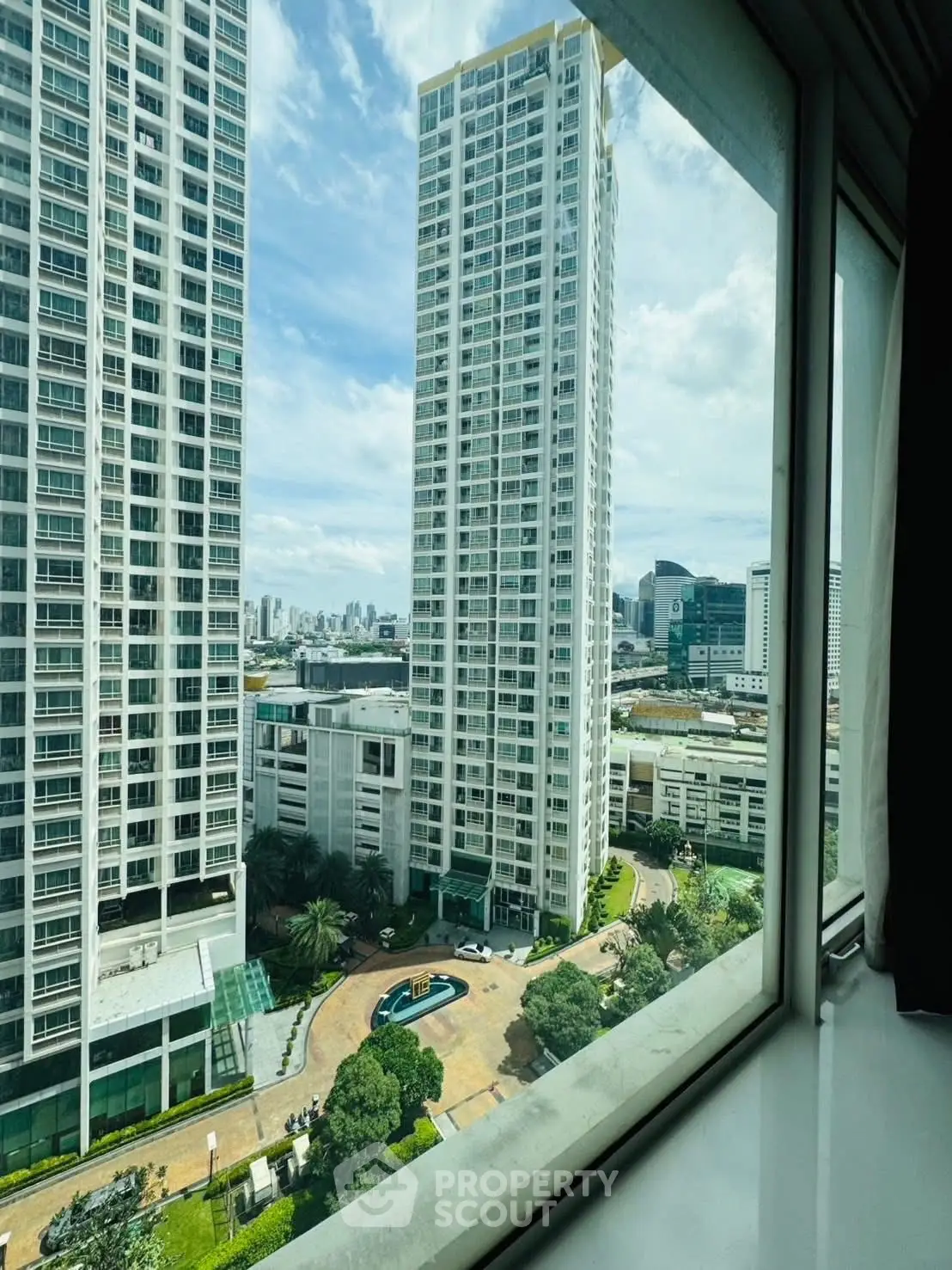 Stunning cityscape view from high-rise apartment window, showcasing modern architecture and lush greenery.