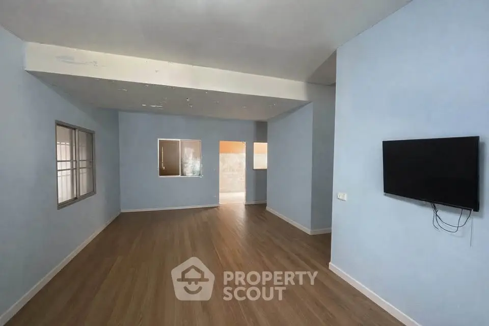 Spacious empty living room with wooden flooring and wall-mounted TV, perfect for customization.